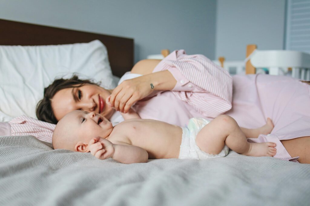 une maman est allongée dans un lit et joue avec son bébé