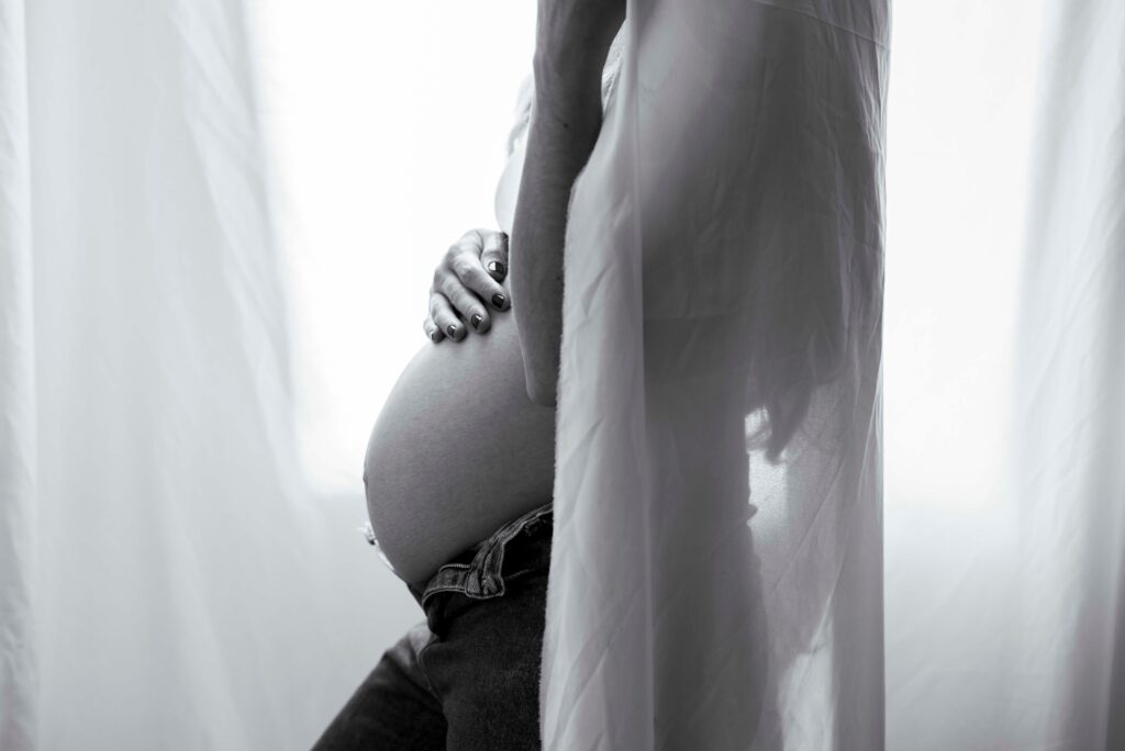 photo en noir et blanc d'une femme enceinte devant une fenêtre