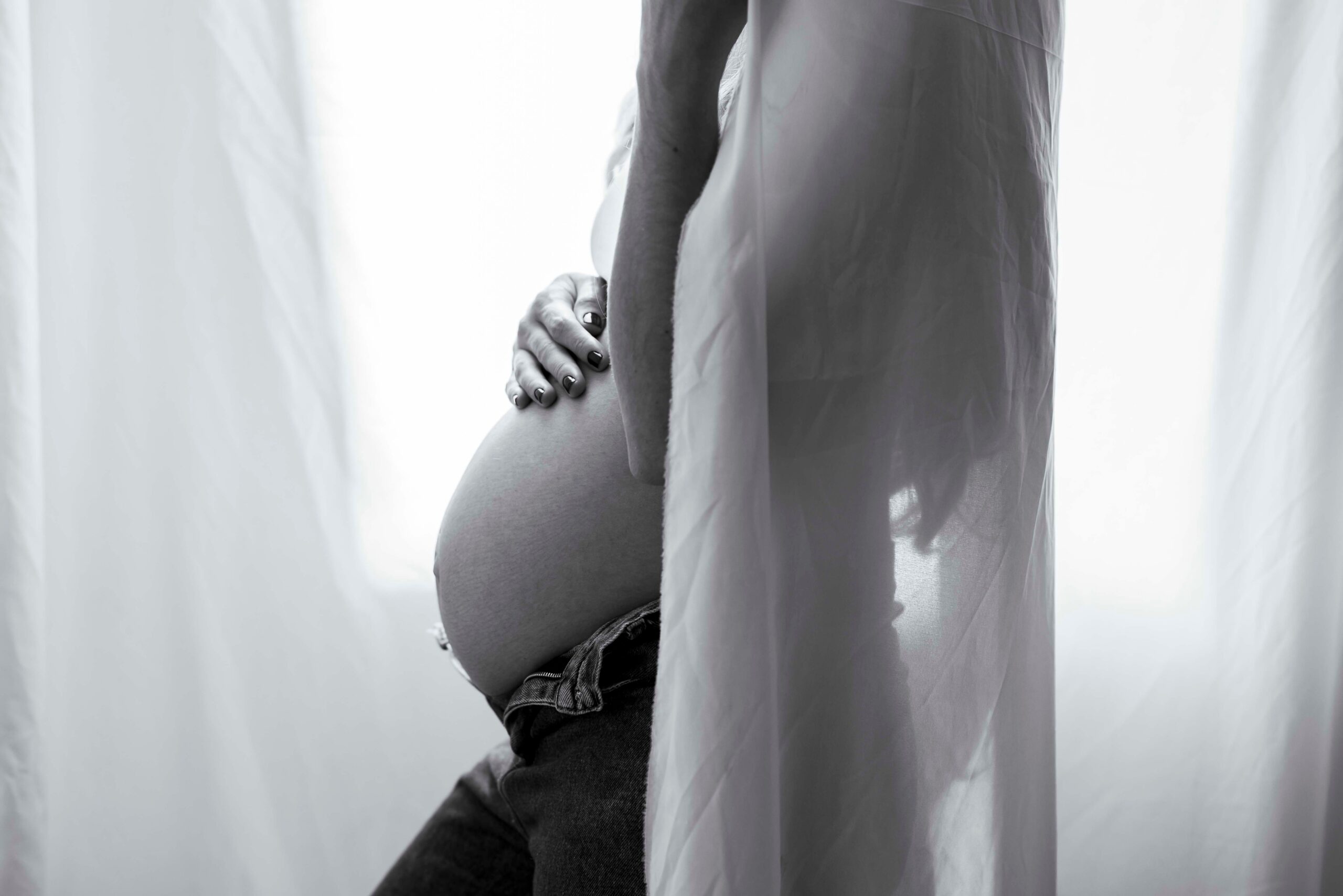photo en noir et blanc d'une femme enceinte devant une fenêtre